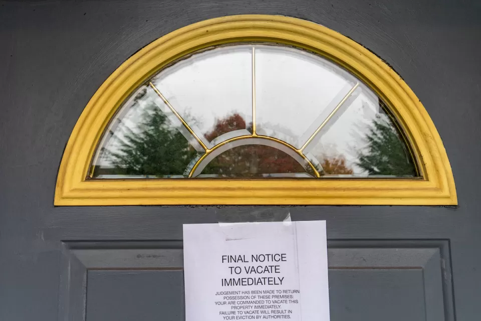 Eviction notice taped to dark grey door with arched window at top.